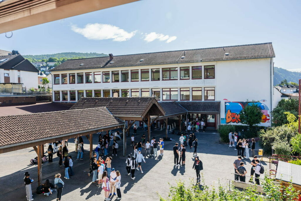 Schülerinnen und Schüler verbringen die Pause auf dem sonnigen Schulhof