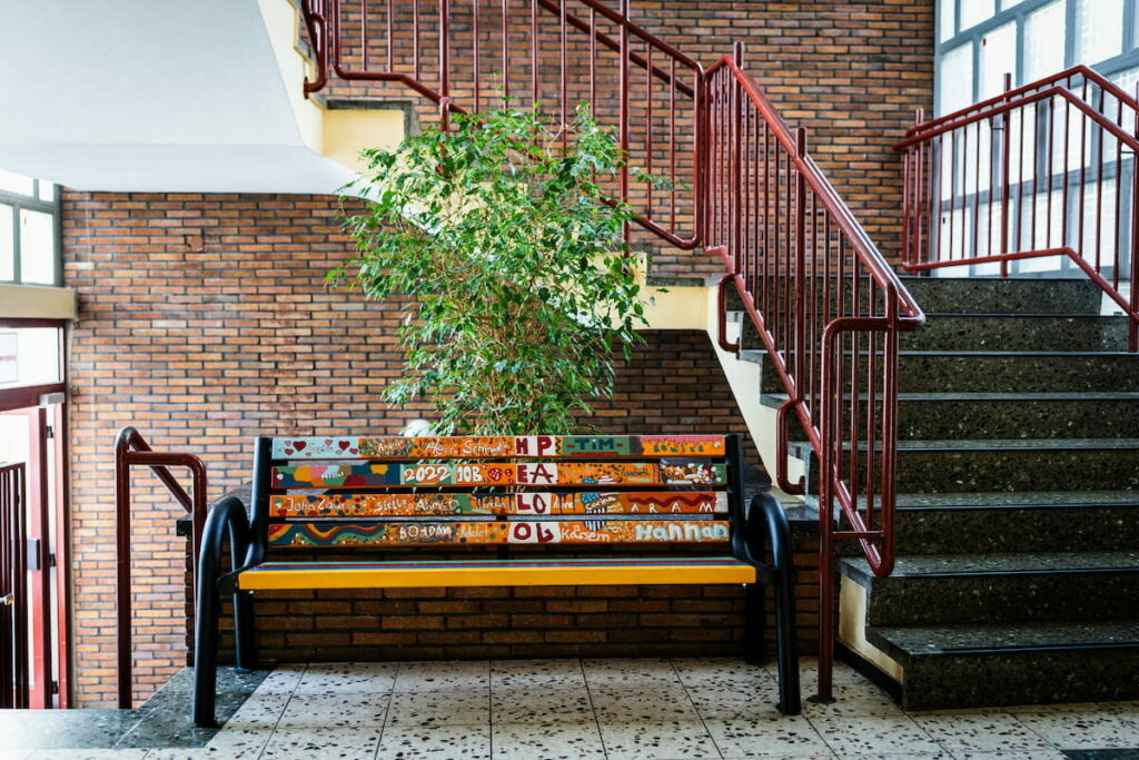 Innenansicht. Eine bunt bemalte Sitzbank im Treppenhaus