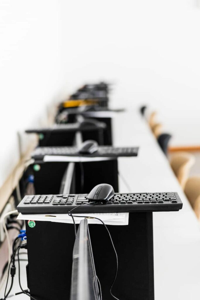 Mehrere Computer stehen in einer Reihe. Darauf liegen jeweils Maus und Tastatur